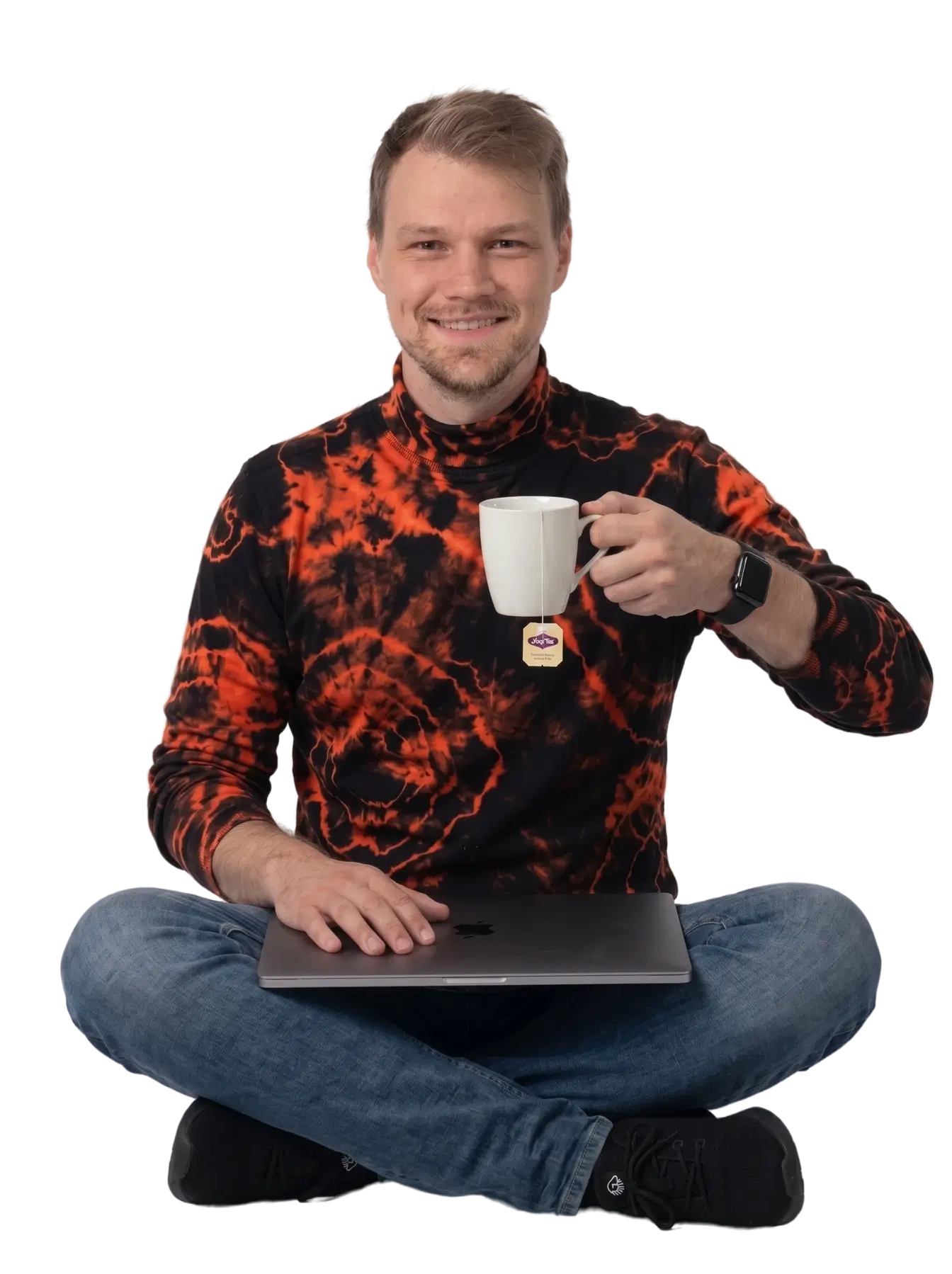 Christopher Matt, Entwickler von WP Dashlytics, sitzt im Schneidersitz mit zugeklapptem MacBook auf dem Schoß und einer Tasse Tee in der Hand. Er lächelt erleichtert und trägt einen schwarzen Rollkragenpullover mit orangem Batik-Effekt.